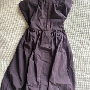 Mörklila axelbandslös klänning - Säljer en mörklila axelbandslös klänning med smockad rygg och dragkedja framtill.Perfekt för dig som gillar en enkel men snygg look med lite volym i kjolen. Storlek m men passar även mindre storlekar