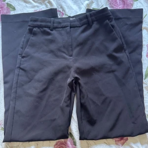 Svarta kostymbyxor från H&M - Klassiska svarta kostymbyxor från H&M med raka ben och hög midja. Byxorna har hällor för bälte, snedställda fickor fram och dekorativa fickor bak. Snygg passform och stilren look, perfekta till skjorta eller t-shirt.