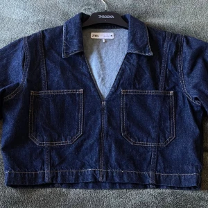 Denim tröja Zara  - Snygg mörkblå croppad jeansjacka från Zara med två stora fickor framtill och markerade sömmar. Jackan har klassisk krage, v-ringning och långa ärmar. Nyskick