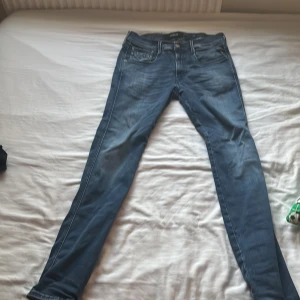 Replay Anbass jeans blå, stl 31 - Säljer ett par snygga Replay Anbass jeans i klassisk blå tvätt. Modellen är slim och har en modern passform med smala ben. Jeansen har fem fickor, dragkedjegylf och detaljer i läder vid linningen. Perfekta för dig som gillar stilrena och bekväma jeans.