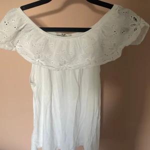 Vit offshoulder blus 🤍🤍 - Superfin vit blus från Hampton Republic med offshoulder-modell och bred volang upptill. Blus har broderade blommor och hålmönster på volangen, vilket ger en romantisk och somrig känsla. Perfekt för varma dagar och snygg till sneakers eller sandaler. Älskarr💘💘
