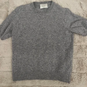 Grå stickad tröja från Neo Noir - Mysig grå stickad tröja från Neo Noir med rund hals och korta ärmar. Tröjan har en enkel och stilren design med ribbade muddar vid hals, ärmslut och nederkant. Perfekt för lager-på-lager under hösten och vintern.