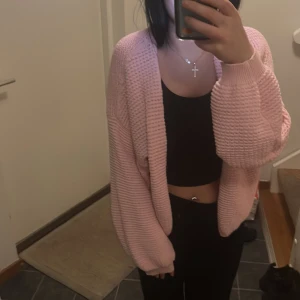 Ljusrosa stickad kofta - Säljer en mysig ljusrosa stickad kofta med grov struktur och långa ärmar. Koftan har en loose passform och är öppen framtill utan knappar eller dragkedja. Perfekt att slänga över en crop top för en chill look.