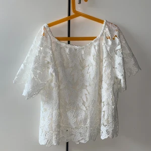 Vit spetsblus från H&M, stl 40 - Superfin vit blus från H&M i storlek 40, med breda korta ärmar och offshoulder-modell. Blusen är täckt av blommig spets med snygga detaljer och har en luftig känsla. Perfekt för dig som gillar romantisk och somrig stil.