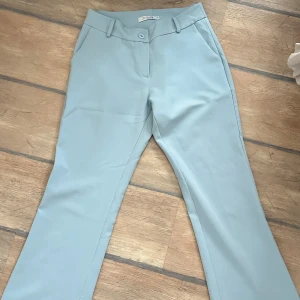 Ljusblå bootcut kostymbyxor - Snygga ljusblå kostymbyxor från designbysi med bootcut-snitt. Byxorna har klassiska fickor fram, bälteshällor och stängs med knapp och dragkedja. Perfekta för en clean och stilren look.