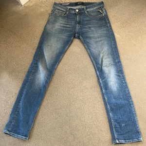 Replay blå jeans 30/32 herr - Snygga blå jeans från Replay i klassisk tvätt med lätt slitning. Modellen är Rocco och har raka ben och fem fickor, tillverkade i ekologisk bomull. Perfekta för dig som gillar en tidlös och avslappnad stil.