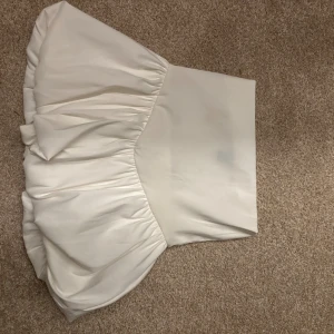 Vit volangtopp - Supersöt vit topp med volang. Toppen har en fluffig, voluminös form och är perfekt för dig som vill sticka ut. Materialet känns mjukt och har en lätt glans. Passar perfekt till ett par jeans och sneakers.