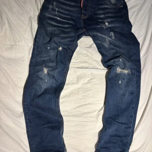 Dsquared2 jeans - Snygga blå jeans från Dsquared2 med skinny passform. Jeansen har slitna detaljer, färgstänk och en klassisk femficksdesign. Tydlig Dsquared2-logga vid gylfen. Perfekta för dig som gillar en edgy och trendig look.