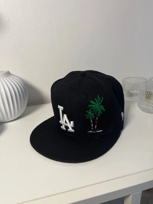 Svart LA Keps strl 55,8 - Svart LA Keps med palmträd som design. Strl 55,8