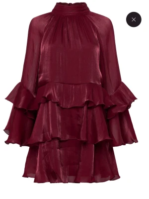 Vinröd volangklänning med rosett - Säljer en vinröd kortklänning med flera lager volanger och långärmade, vida ärmar. Klänningen har hög hals och en stor rosett i nacken. Använd 1 gång och köptes för ca en vecka sedan. 