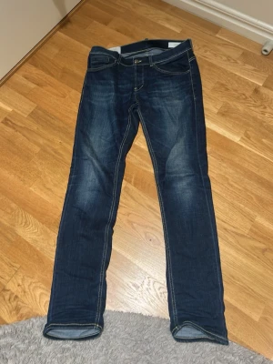 Dondup blå jeans, storlek 34 - Säljer ett par snygga blå Dondup George i storlek 34. Jeansen har klassisk femficksdesign, kontrastsömmar och raka ben med en straight passform. Materialet är slitstarkt jeans och färgen är mörkblå med lätt tvättade detaljer. Dessa är använda 5 gånger max. Jag tröttnade på tighta jeans och vill därför sälja. Skriv om du vill få reda på något mer om de. 