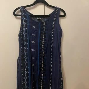 Blåmönstrad klänning från Group - Säljer en kort klänning från Group i olika blå nyanser med vita inslag. Klänningen har ett unikt randigt och mönstrat tryck, är ärmlös och har ett band i midjan för att knyta till önskad passform. Perfekt för dig som gillar bohemiska vibes och vill sticka ut. Finns ingen storlek men gissar på xs/s 
