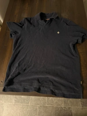 Svart polotopp från Morris Stockholm - Klassisk svart polotopp från Morris Stockholm i storlek S. Toppen har korta ärmar, krage och en liten broderad logga på bröstet. Materialet känns mjukt och är troligen bomull.