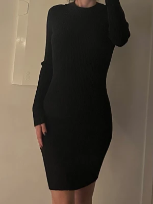 Svart stickad klänning  - Snygg svart stickad klänning med lång ärm och rund hals. Modellen är kort och har en slim passform som framhäver figuren. Inköp BikBok storlek S passar även xs