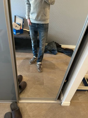 Replay Anbass  - Säljer ett par Replay Anbass jeans i blå tvätt med snygga slitningar och klassiska fem fickor. Jeansen har rak passform och normal midja, med Replay-logga på bakfickan. Materialet är slitstarkt denim i bomull. Perfekt för dig som gillar en avslappnad stil.