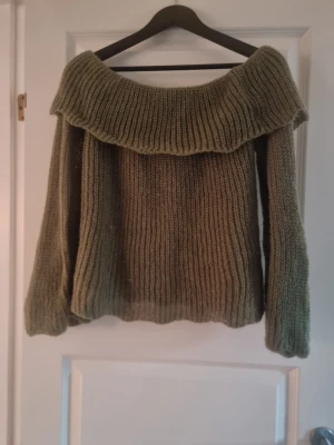Olivgrön stickad offshoulder tröja - Säljer en olivgrön stickad tröja med bred offshoulder-krage. Tröjan har grov ribbstickning och långa ärmar med lite loose passform. Perfekt för dig som gillar chill och snygg stil med en twist. Materialet är mjukt och värmande stickat garn.