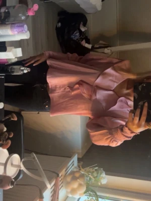 Satinblus Neo Noir - Rosa satinblus från Neo Noir i en elegant, feminim modell. Blusen har en vacker volangkant längs halsringningen som ger ett lyxigt fall, samt långa ärmar med bred smock vid handlederna för en fin siluett. Tyget är mjukt, glansigt och faller supersnyggt.