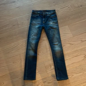Blå skinny jeans från Nudie Jeans - Säljer ett par blå skinny jeans från Nudie Jeans med slitna detaljer och kontrastsömmar. Jeansen har klassisk femficksmodell, normal midja och är tillverkade i jeansmaterial. Perfekta för dig som gillar en smal passform och cool tvätt.