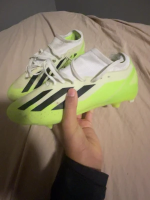 Adidas fotbollsskor i neon och vitt - Säljer ett par Adidas fotbollsskor i neon-gul och vit med svarta ränder på sidan. Skorna har snörning och en strumpliknande ovandel för extra komfort. Sulan har fasta dobbar och är gjord för spel på gräs. Använd en gång Perfekt för dig som vill sticka ut på planen. Strl 43 och är i pros model. Nypris 1800kr. Hör gärna av dig om du har några frågor eller liknande🙌