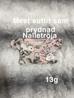 Rosa blommig nalletröja från Newbie - Supergullig rosa nalletröja från Newbie med blommigt mönster och söta djurmotiv som kanin och fågel. Perfekt för att ge din nalle eller docka en extra söt look. 🌸 Använd mest som prydnad. Liten nalletröja.