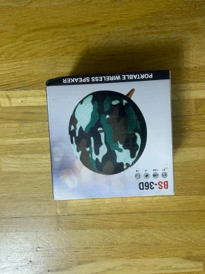 BS-360D Portable Wireless Speaker - BS-360D är en portabel trådlös högtalare med kamouflagemönster. Den har Bluetooth, FM-radio, USB och TF-kortstöd. Batterikapacitet på 800mAh, upp till 4 timmars speltid. Lådan har mindre skador men produkten är ny i förpackning.