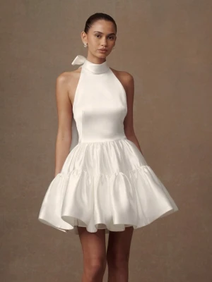 Vit kort halterneckklänning med rosett - Supersöt vit kort klänning i satin med halterneck och stor rosett i nacken. Säljs som bröllopsklänning på Meshki. Nypris ca 3000kr. Aldrig använd med prislappen kvar. En trådreva fram på bröstet som inte syns mycket på avstånd, se sista bilden. 