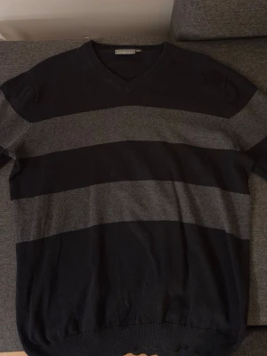 Randig tröja Race Marine, svart/grå - Snygg stickad tröja från Race Marine i storlek L. Tröjan har breda svarta och gråa ränder, v-ringad hals och långa ärmar. Perfekt för dig som gillar en klassisk men chill stil. Passar bra till jeans eller chinos.
