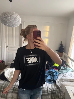 Svart Nike Dri-Fit t-shirt - Svart t-shirt från Nike med stor vit logga framtill i en cool box-design. Tillverkad i Dri-Fit-material som andas och känns lätt mot huden. Klassisk passform med korta ärmar och rund hals. Perfekt för dig som gillar sportig och avslappnad stil.