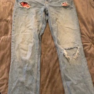 Ljusblå slitna jeans  - Ljusblå jeans med snygga slitningar och hål på båda benen för en cool och avslappnad look. Klassisk femficksmodell med raka ben och normal passform. Perfekt för dig som gillar streetstyle och vintage vibe. Pris kan diskuteras och köparen står för frakt (den har en liten fläck på benet på andra bilden som jag inte vet om den försvinner i tvätten eller inte)