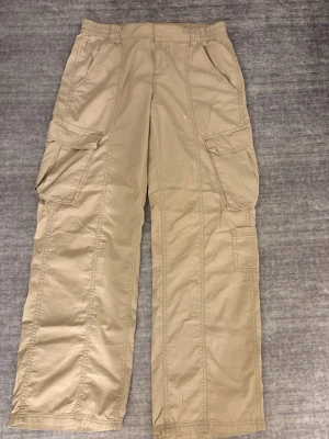 Beiga cargopants med fickor - Säljer ett par beiga cargopants med flera praktiska fickor på sidorna. Byxorna har en loose passform.