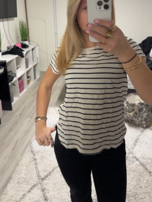 Randig t-shirt från H&M Basics - Vit t-shirt från H&M Basics med svarta horisontella ränder. Klassisk rund halsringning och korta ärmar. Skön och lätt i bomull, perfekt till jeans eller shorts. Enkel och tidlös stil som funkar året runt.