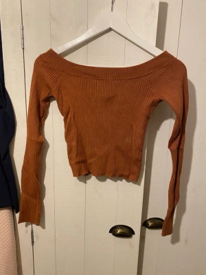 Rostbrun offshoulder topp Bik Bok - Säljer en snygg rostbrun ribbad offshoulder topp från Bik Bok i storlek S. Toppen har lång ärm och är croppad med en bred halsringning som sitter snyggt över axlarna. Perfekt att styla med jeans eller kjol för en trendig look.
