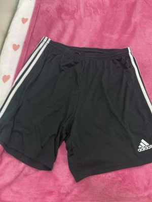 Svarta Adidas shorts med vita ränder - Säljer ett par svarta Adidas shorts. Storleken är 2xl men skulle säga att den även pssar L då denr stretchig.