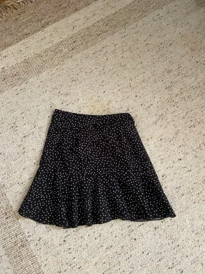 Svart prickig kjol från SHEIN - Säljer en svart kortkjol från SHEIN med vita prickar. Kjolen har en lätt utsvängd form och sitter snyggt i midjan. Materialet är mjukt och känns skönt mot huden, perfekt för dig som gillar trendiga mönster och vill ha en kjol som sticker ut.