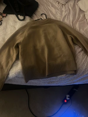 Beige stickad tröja med ribbad kant - Säljer en beige stickad tröja med rund hals och breda ribbade muddar vid ärmslut och nederkant. Tröjan har en loose passform och långa ärmar, perfekt att slänga på sig när det är lite kyligt ute. Enkel och stilren design som funkar till allt.