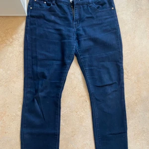 Mörkblå jeans från BS Fashion, stl 42 - Snygga mörkblå jeans från BS Fashion i klassisk femficksmodell. Jeansen har en smal passform, dragkedja och knapp framtill samt dekorativa nitar och detaljer på bakfickan. Materialet är en mix av bomull, polyester och elastan för extra stretch och komfort.