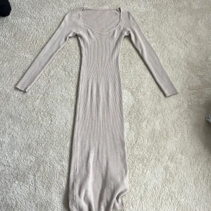 Beige ribbad långklänning med slits - Supersnygg beige ribbad långklänning med lång ärm och rundad urringning. Klänningen har en tight passform och en slits bak. Står inte storlek men skulle gissa på xs-s