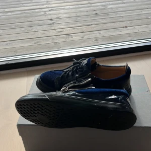 Guiseppes blå mocka - Snygga sneakers i mörkblå mocka med svarta lackdetaljer och coola silverfärgade dragkedjor på sidorna. Skorna har svarta snören och en platt svart sula. Perfekta för dig som vill sticka ut med en unik och trendig look. Har 42 i storlek och har kunnat ha på mig dom utan problem 
