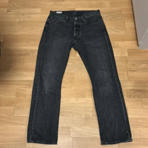 Levi's 501 svarta jeans W32 L32 - Svarta Levi's 501 jeans i klassisk rak modell. Jeansen är tillverkade i slitstarkt denim och har fem fickor, knappgylf och snygga kopparfärgade nitar. Perfekta för dig som gillar en tidlös och clean look.