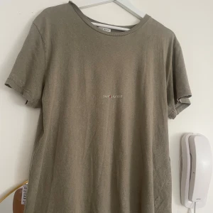 Grön t-shirt från Saint Laurent - Säljer denna snygg t-shirt från Saint Laurent. Färgen är grön/khaki med en ”sliten” look. Rund halsringning och avslappnad passform.