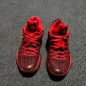 Röda Nike KD sneakers med snörning - Säljer ett par röda Nike KD sneakers med svart och röd stickad ovandel, vita swoosh-loggor på sidorna och KD-logga på plösen. Skorna har snörning och platt sula, perfekta för dig som gillar sportig stil och vill sticka ut med färg.