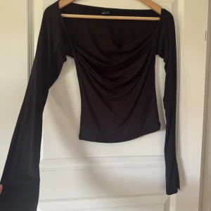 Svart långärmad topp Gina Tricot S - Svart långärmad topp från Gina Tricot i storlek S. Toppen har en snygg draperad front och bred, rak urringning. Tillverkad i ett mjukt och stretchigt material som sitter skönt på kroppen. Perfekt att styla med jeans eller kjol.