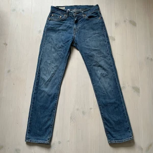 Levi's 511 blå jeans W28 L30 - Säljer ett par klassiska Levi's 511 jeans i blå denim. Modellen har en slim passform med raka ben och fem fickor. Snygga kontrastsömmar och läderpatch bak i midjan. Perfekta för dig som gillar en tidlös och stilren look.