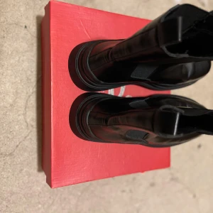 Svarta chelsea boots i skinn - Snygga svarta chelsea boots med rund tå och platt sula. Skorna är i skinn med elastiska paneler på sidorna och dragflikar upptill för enkel påtagning. Perfekta för dig som gillar en stilren och chunky look.