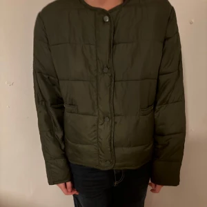 Olivgrön pufferjacka från Zara - Säljer en olivgrön pufferjacka från Zara i storlek S. Jackan har rund halsringning, tryckknappar framtill och två fickor. Den är quiltad och har en boxig, lite loose passform. Perfekt för kyligare dagar och enkel att styla till jeans eller hoodies.