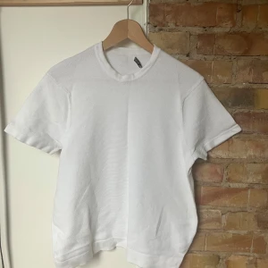 Vit t-shirt från ZARA - Klassisk vit t-shirt från ZARA i storlek S. T-shirten har korta ärmar, rund halsringning och är tillverkad i ett strukturerat bomullstyg som ger en snygg och stilren look. Perfekt till jeans eller shorts för en clean vibe.