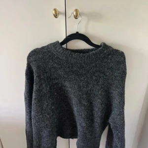 Mörkgrå stickad tröja - Mysig mörkgrå stickad tröja med rund halsringning och långa ärmar. Perfekt för kyliga dagar och enkel att matcha med jeans eller kjol. Tröjan har en något lös passform och är tillverkad i ett mjukt, värmande material.