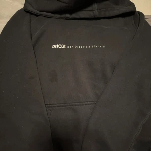 Svart hoodie från DirtCult - Svart hoodie från DirtCult med tryck 'San Diego California' på bröstet. Klassisk känguruficka framtill och huva. Perfekt för dig som gillar streetwear och enkel stil. I storlek M men krympt i tvätten så skulle säga att den är i S. Köpt för 800