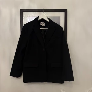 Svart kavaj från NA-KD - Klassisk svart kavaj från NA-KD med enkelknäppning och två fickor framtill. Rak passform och snygg krage. Perfekt att styla med skjorta eller t-shirt för en clean look. Fodrad insida för extra komfort.