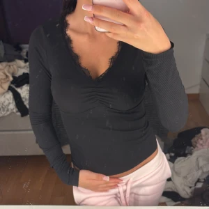 Svart ribbad topp med spetsdetalj - Säljer en svart långärmad topp med ribbad struktur och v-ringning med spetskant i stolek xs